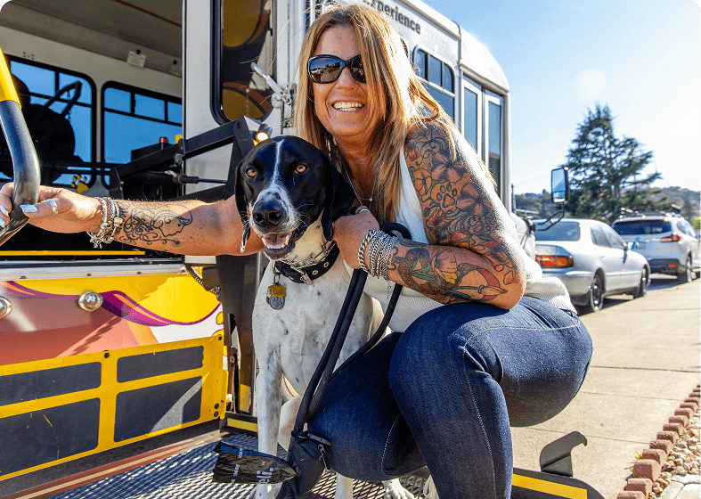 Woman with dog beside a colorful bus.